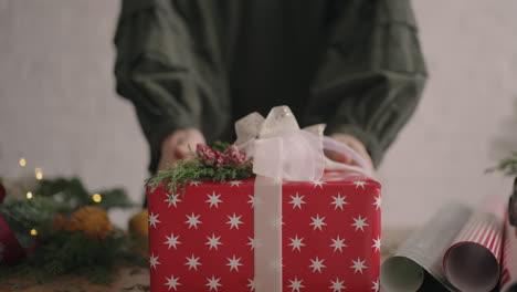 The-camera-follows-the-gift.-A-woman-with-her-hands-pushes-a-Christmas-box-with-decorations-into-the-camera.-Green-Christmas-gift-made-with-your-own-hands-from-eco-friendly-materials