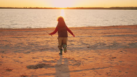 happy-little-boy-is-running-over-sandy-beach-of-river-in-sunset-childhood-moment-and-happiness