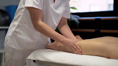 Anonymous-female-physiotherapist-massaging-leg-of-crop-woman