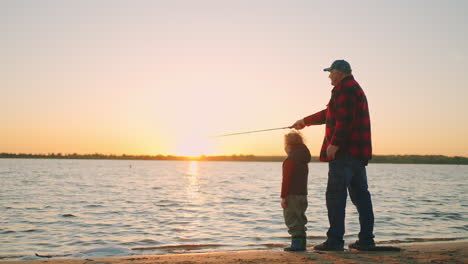 happy-father-and-son-are-fishing-on-river-shore-in-sunset-old-man-and-little-child