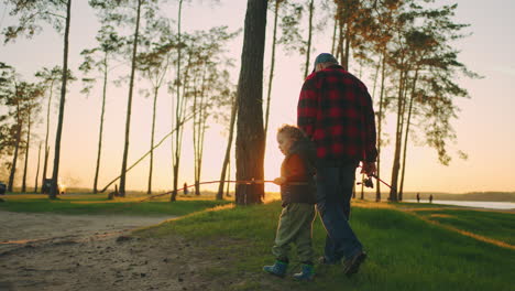 grandpa-and-grandson-are-walking-together-in-forest-or-natural-park-in-sunset-time-going-to-fishing-on-river-shore