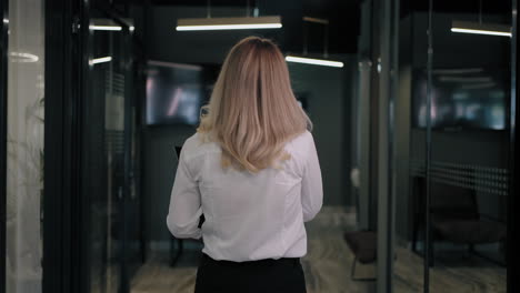 The-camera-follows-the-corridor-behind-a-blonde-in-a-white-shirt-of-a-business-woman