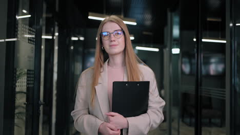 Portrait-of-a-business-woman-with-glasses-walking-down-the-corridor-of-a-business-center-with-papers
