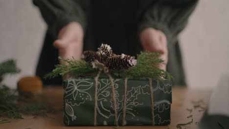 The-camera-follows-the-gift.-A-woman-with-her-hands-pushes-a-Christmas-box-with-decorations-into-the-camera.-Beautiful-Christmas-gift-made-with-your-own-hands-from-eco-friendly-materials