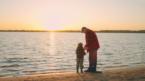 little-boy-is-spending-time-with-grandfather-in-fishing-old-man-is-giving-fishing-rod-to-child