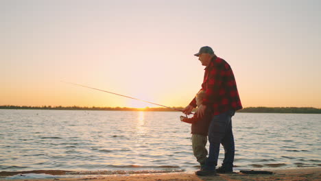 Alter-Fischer-Bringt-Seinem-Enkel-Das-Fischen-Bei-Großvater-Und-Kleines-Kind-Stehen-Am-Ufer