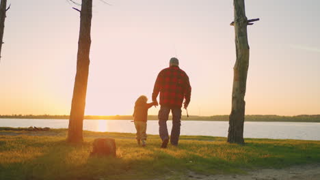 old-man-and-his-grandson-are-travelling-in-nature-walking-to-lake-for-fishing-in-sunset-rear-view