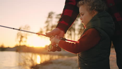 fishing-on-shore-of-river-or-lake-in-sunset-little-boy-is-catching-fish-by-rod-father-or-granddad-is-helping