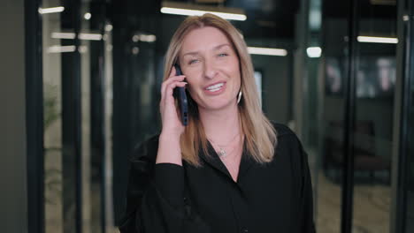 Smiling-businesswoman-looking-on-cellphone-indoors.-Surprised-business-woman-reading-message-on-mobile-phone-in-office-corridor.-woman-looking-smartphone-screen-in-business-center.-walking-office