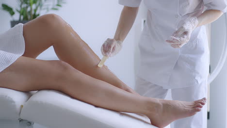 Use-a-stick-to-apply-a-moisturizing-gel-on-the-client's-legs-before-laser-hair-removal-on-the-legs.-The-doctor-prepares-his-legs-for-laser-hair-removal-in-a-beauty-salon