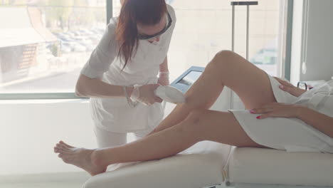 laser-or-IPL-hair-removal-technology-in-contemporary-beauty-clinic-cosmetologist-is-using-apparatus-on-skin-of-legs