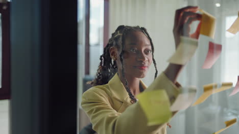 African-American-Business-Woman-Write-Tasks-Creative-Ideas-On-Sticky-Notes-On-Glass-Board-Female-Corporate-Leader-Planning-Project-On-Post-It-Sticky-Notes-Organize-Work-On-Stickers