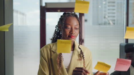 African-American-Business-Woman-Write-Tasks-Creative-Ideas-On-Sticky-Notes-On-Glass-Board-Female-Corporate-Leader-Planning-Project-On-Post-It-Sticky-Notes-Organize-Work-On-Stickers