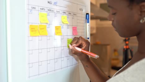 Crop-black-woman-taking-notes-in-planner-on-fridge