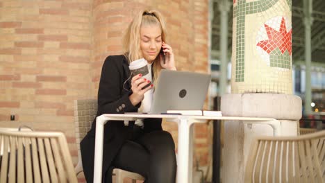 Mujer-Hablando-Por-Teléfono-Inteligente-Mientras-Trabaja-Con-Una-Computadora-Portátil-En-La-Cafetería