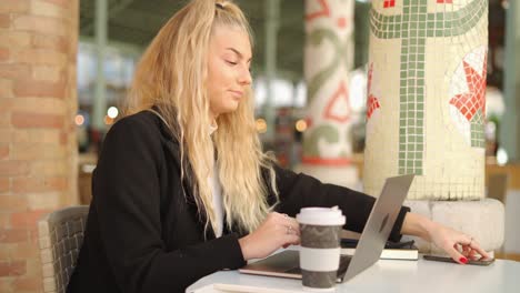 Woman-talking-on-smartphone-while-working-with-laptop-in-cafe