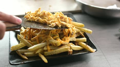 Crop-cook-adding-pulled-chicken-on-pile-of-French-fries
