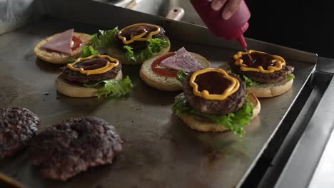 Anonymous-cook-preparing-tasty-hamburgers-and-adding-sauce