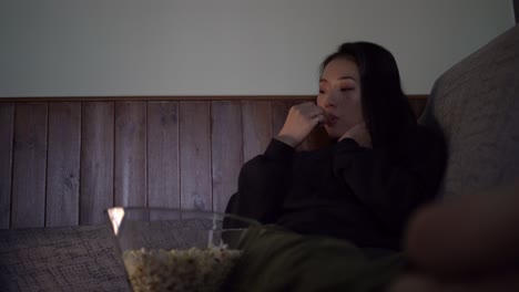 Young-Asian-woman-sitting-on-sofa-and-eating-popcorn