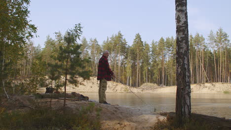 lonely-man-is-fishing-on-shore-of-river-in-forest-at-sunny-morning-resting-at-vacation-standing-with-rod-in-hand