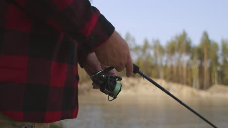 fisherman-is-rotating-reel-of-fishing-rod-closeup-view-of-hands-angling-and-spin-fishing-in-lake-of-forest