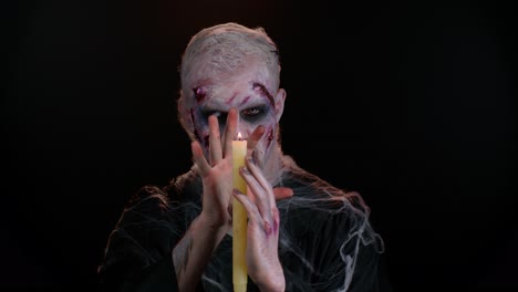 Hombre-Con-Maquillaje-Zombie-Sangriento-Herido-De-Halloween,-Tratando-De-Asustar,-Hechizos-Evoca-Sobre-Una-Vela