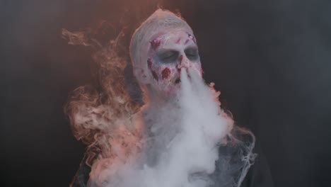 Zombie-man-with-makeup-with-wounds-scars-and-white-contact-lenses-blows-smoke-from-nose-and-mouth