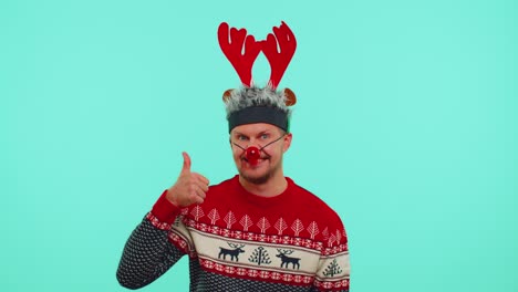 Funny-man-wears-red-New-Year-sweater-deer-antlers-raises-thumbs-up-agrees-with-something-good,-like