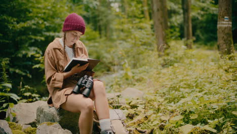 Mujer-Escribiendo-En-Un-Libro-Sentado-Sobre-Una-Roca-En-El-Bosque
