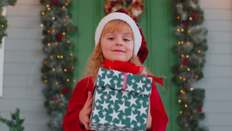 Happy-toddler-child-girl-kid-in-red-sweater-gifting-one-Christmas-present-box,-stretches-out-hands