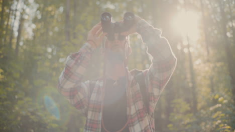 Young-Man-Looking-Through-Binocular-Standing-In-Forest