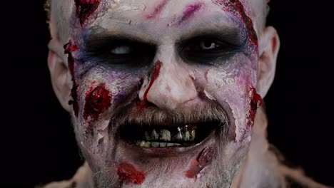 Zombie-man-face-makeup-with-wounds-scars-and-white-contact-lenses-looking-at-camera,-trying-to-scare