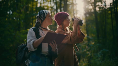 Female-Friends-With-Book-And-Binocular-Exploring-Woods