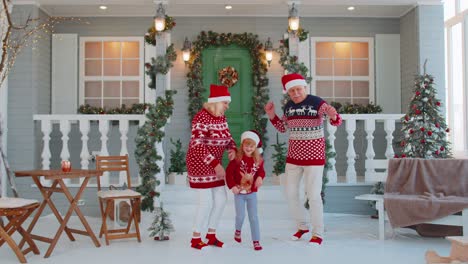 Happy-senior-old-couple-grandparents-with-granddaughter-celebrating-dancing-near-Christmas-house