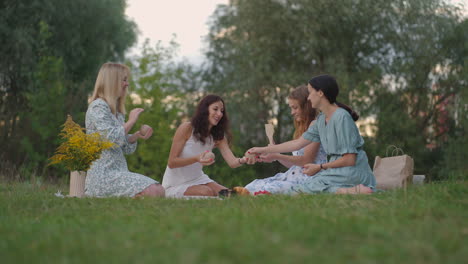A-group-of-young-women-in-nature-in-the-park-hold-a-master-class-in-clay-modeling.-Joint-activity-communication-laughter-common-hobby-women's-circle-creative-activities.
