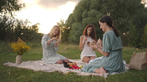 A-group-of-young-women-concentrates-on-drawing-patterns-on-clay-products-with-the-help-of-tools-decorate-molded-objects-in-a-meadow-in-nature-in-an-open-space.-General-view