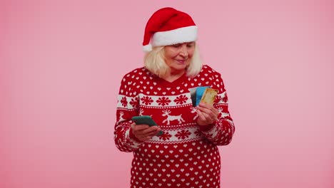 Christmas-grandmother-using-credit-bank-card,-smartphone-while-transferring-money-shopping-online