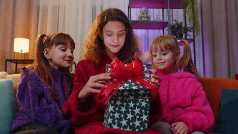 Three-siblings-children-girls-opening-gift-box-with-excited-surprised-face,-birthday-glowing-present