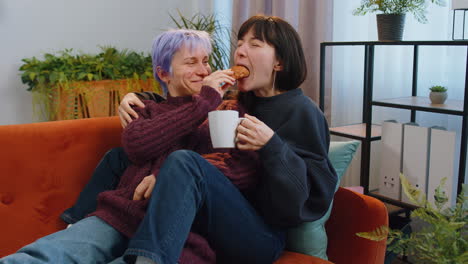 Two-lesbian-women-family-couple,-girl-friends-drinking-coffee,-eating-croissants-and-talking-at-home