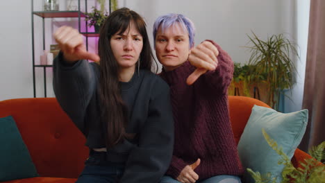 Upset-lesbian-women-family-couple-showing-thumbs-down-sign-gesture-expressing-discontent-disapproval