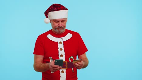 Man-in-Christmas-t-shirt-using-credit-bank-card,-smartphone-while-transferring-money-shopping-online