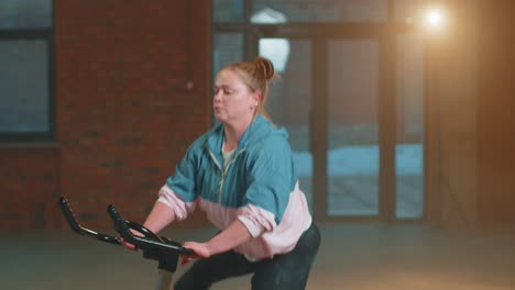 Healthy-Caucasian-woman-exercising-workout-on-stationary-cycle-machine-bike-in-gym,-Slow-Motion