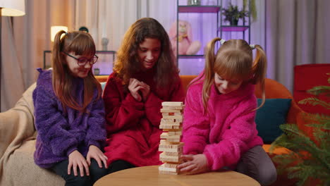 Drei-Geschwister-Kinder-Mädchen-Spielen-Mit-Blöcken-Brettspiel,-Bauen-Zu-Hause-Einen-Turm-Aus-Holzbausteinen