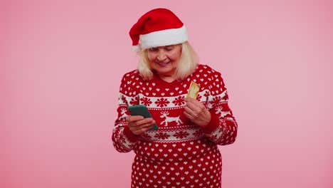 Ältere-Weihnachtsgroßmutter-Mit-Kreditkarte-Und-Smartphone,-Die-Geld-Beim-Online-Einkauf-überweist