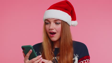 Frau-Im-Stilvollen-Weihnachtspullover-Schaut-Auf-Das-Smartphone-Display-Und-Freut-Sich-Aufrichtig-über-Den-Sieg,-Den-Erfolg-Und-Das-Glück