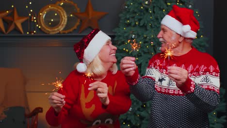 Happy-mature-family-couple-in-festive-clothes-waving-sparklers-bengal-lights-at-home,-Christmas-eve