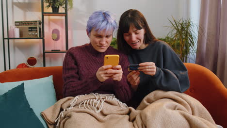 Lesbische-Verheiratete-Frauen-Nutzen-Kreditkarte-Und-Smartphone,-Während-Sie-Geld-Beim-Online-Einkauf-überweisen