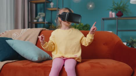 Toddler-girl-sitting-on-home-sofa-using-virtual-reality-headset-helmet-app-to-play-video-3D-game