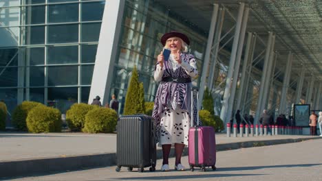Elderly-retired-woman-tourist-near-airport-terminal-celebrating-success,-winning-and-goal-achievemen