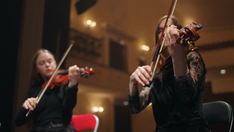 two-female-violinists-are-playing-music-on-scene-of-old-opera-house-orchestra-in-theater